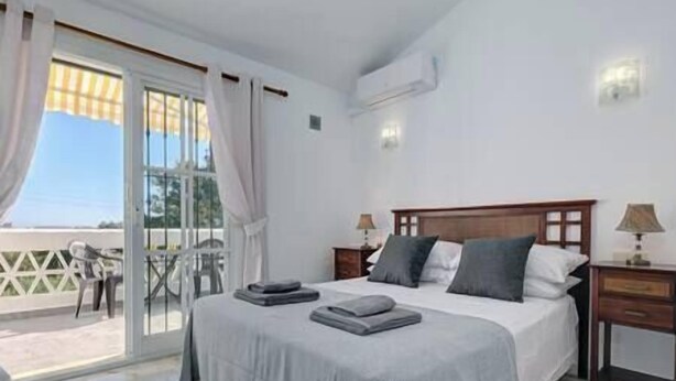 A bedroom with a bed, two bedside tables, a window with curtains, and a view of the outside.