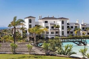 A resort with multiple white buildings, a pool, and palm trees. - Brand New, Luxurious Ground Floor Apartment (Estepona)