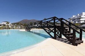 A swimming pool with a wooden bridge and steps leading to a poolside area. - Brand New, Luxurious Ground Floor Apartment (Estepona)