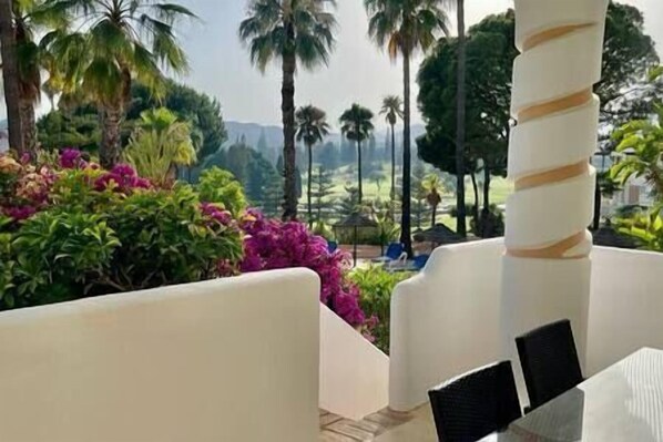 A seating area with a view of a landscaped garden with palm trees and flowering plants.
