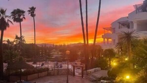 A courtyard with palm trees, a building, and a sunset. - Ground Floor Apartment at Matchroom Country Club (Mijas)
