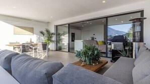 A modern living room with a grey sofa, a wooden coffee table, and a large sliding glass door leading to a kitchen area. - Elegant Two Bedroom Apartment at Estepona Hills! (Estepona)