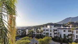 A residential area with white buildings, palm trees, and a mountainous backdrop. - Elegant Two Bedroom Apartment at Estepona Hills! (Estepona)