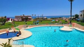 A swimming pool with multiple lanes, a beach in the background, and a few people swimming.