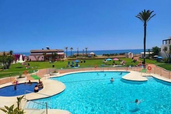 Una piscina con varias pistas de natación, una playa al fondo y algunas personas nadando.