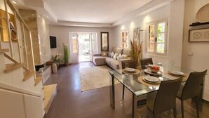 A spacious living area with a sofa, a dining table set for four, and a staircase leading to an upper floor.
