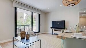 Ein modernes Wohnzimmer mit Glastisch, Flachbildfernseher und Essbereich mit Tisch für zwei Personen.