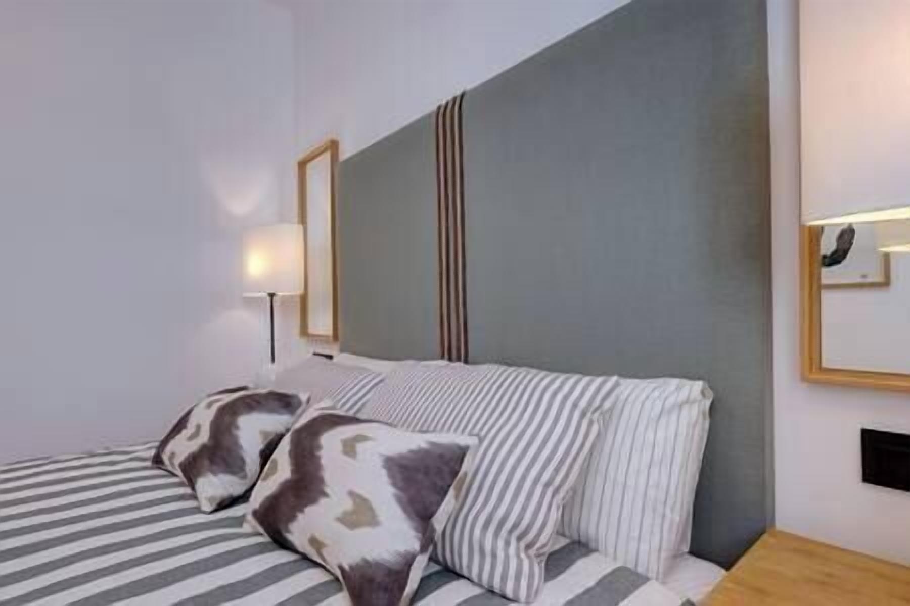 Ett hotellrum med en säng, randiga kuddar, en lampa och en spegel på väggen.