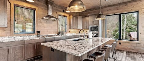 A modern kitchen with a large island, wooden cabinets, and a view of the outdoors.