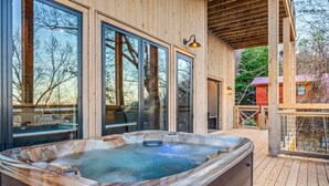 Ein Whirlpool auf einer Holzterrasse mit großen Fenstern, einer Holzpergola und Blick auf Bäume und Gebäude.