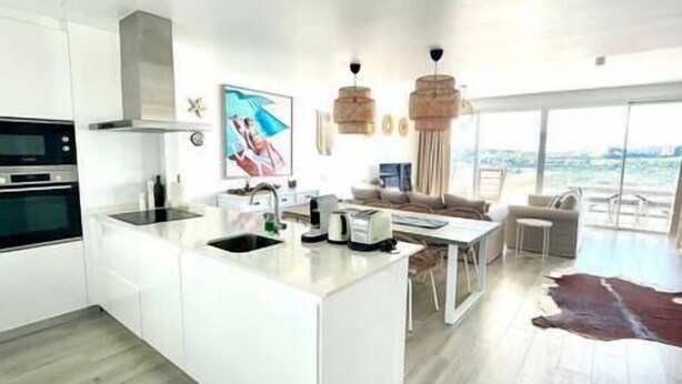 A modern kitchen with a central island, a dining area with a view, and a living space with a large window. - Stunning Three Bedroom Townhouse (Estepona)
