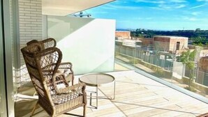 A balcony with a wicker chair and a small round table, overlooking a cityscape with buildings and a clear sky. - Stunning Three Bedroom Townhouse (Estepona)