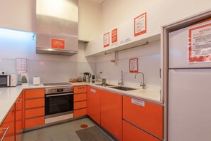 Une cuisine compacte avec des meubles de couleur orange, une cuisinière en acier inoxydable, un four à micro-ondes et un évier.