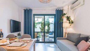 Un salon moderne avec un canapé, une table à manger dressée, un téléviseur et une vue sur la verdure à l’extérieur.