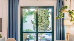Une pièce dotée d’une porte-fenêtre coulissante donnant sur un espace extérieur, d’un canapé, d’une table et d’une plante suspendue.