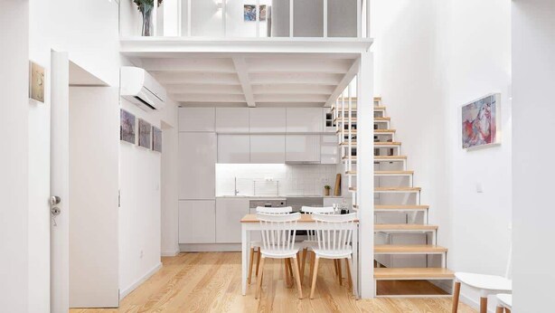 A modern kitchen with white cabinets, a dining area with a table and chairs, and a wooden staircase.