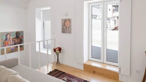 A modern living room with a sofa, a painting, a vase with flowers, and a large sliding glass door leading to an outdoor area.