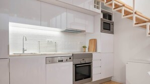 A modern kitchen with white cabinetry, a built-in oven, a microwave, and a wooden cutting board.