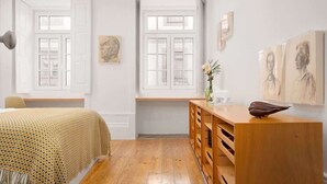 A room with a bed, a wooden dresser, and two windows with white frames.