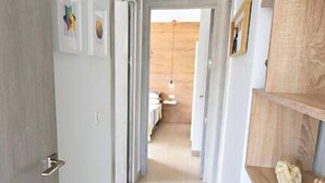 Ein Flur mit einer Holztür, einer weißen Wand mit Bilderrahmen und einem Holzregal mit einem dekorativen Gegenstand.