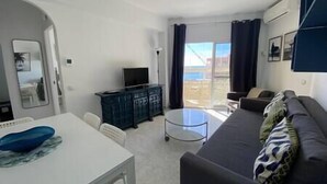 Een woonkamer met een bank, een bijzettafeltje, een televisie en een balkon met uitzicht.