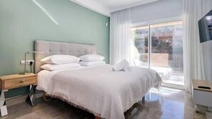 Quarto de hotel moderno com uma cama grande, mesa de cabeceira, televisão e janela com cortinas.