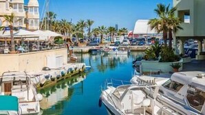 A marina with boats docked, palm trees, and buildings with white domes.