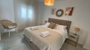 A modern hotel room with a large bed, a chair, a bedside table, and a hanging light fixture.