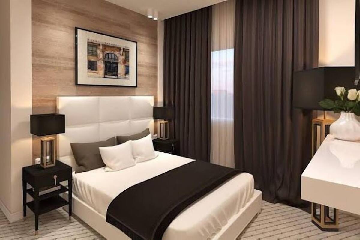 A modern hotel room with a large bed, two bedside tables, a desk, and a painting on the wall.
