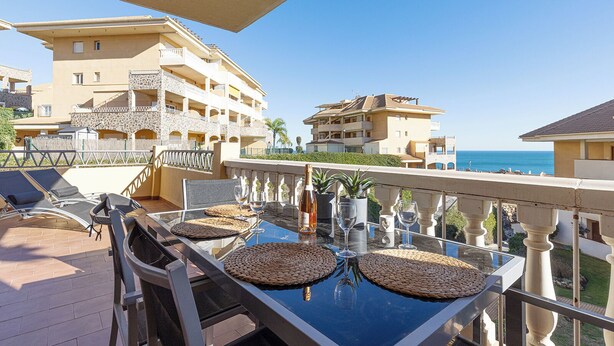 A balcony with a table set for dining, overlooking a coastal area with buildings and the sea. - Spacious 2 bedroom apartment with sea view! (Municipality of Fuengirola)