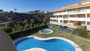 A swimming pool with a circular hot tub, surrounded by a fence, and a building with balconies in the background. - Spacious 2 bedroom apartment with sea view! (Municipality of Fuengirola)