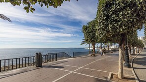 A paved promenade with a railing, trees, and a view of the sea.