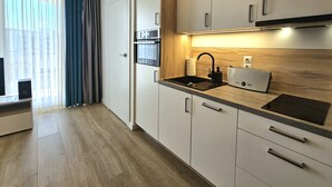 A modern kitchen with white cabinets, a wooden countertop, a built-in oven, a sink, and a coffee machine. - Apartament Pawie Oczko - 365PAM (Kolobrzeg)
