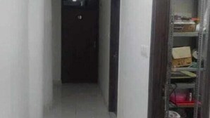 A narrow hallway with a door at the end, a metal shelving unit on the right, and a tiled floor. - Hotel Regal (Saharanpur)