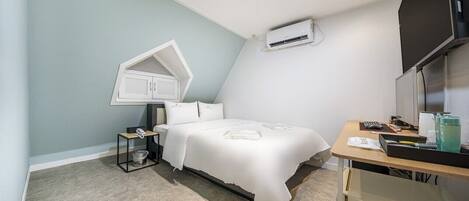 A bedroom with a bed, a desk, an air conditioner, a telephone, and a trash bin.