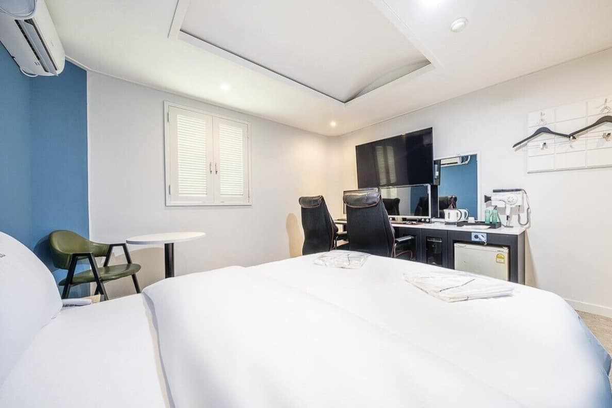 Una habitación de hotel con cama, escritorio, silla, televisor y ventana con persianas.