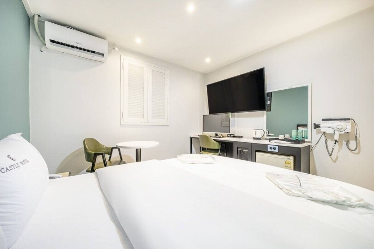 Una habitación de hotel con cama, escritorio, silla, televisión y aire acondicionado.