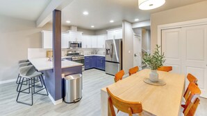 Une cuisine moderne avec des meubles blancs, un réfrigérateur en acier inoxydable et un four à micro-ondes. On y trouve également un coin repas avec une table en bois et des chaises orange.