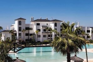 Stunning hotel facade with a symmetrical design, featuring balconies and windows, and a serene pool surrounded by lush greenery.
