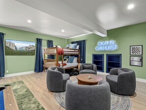 Une chambre moderne avec un lit superposé, des fauteuils gris, une table basse ronde et un panneau lumineux au néon.