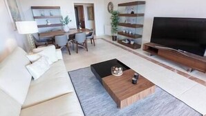 Un salon avec un canapé, une table basse, un téléviseur et des étagères.