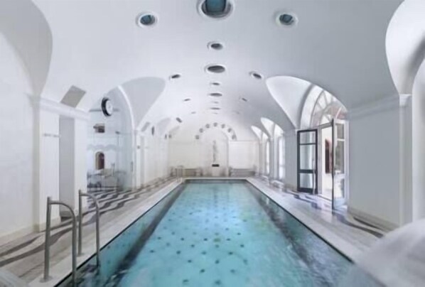 A long, narrow indoor swimming pool with a clear blue water surface, surrounded by white walls and arched ceilings.