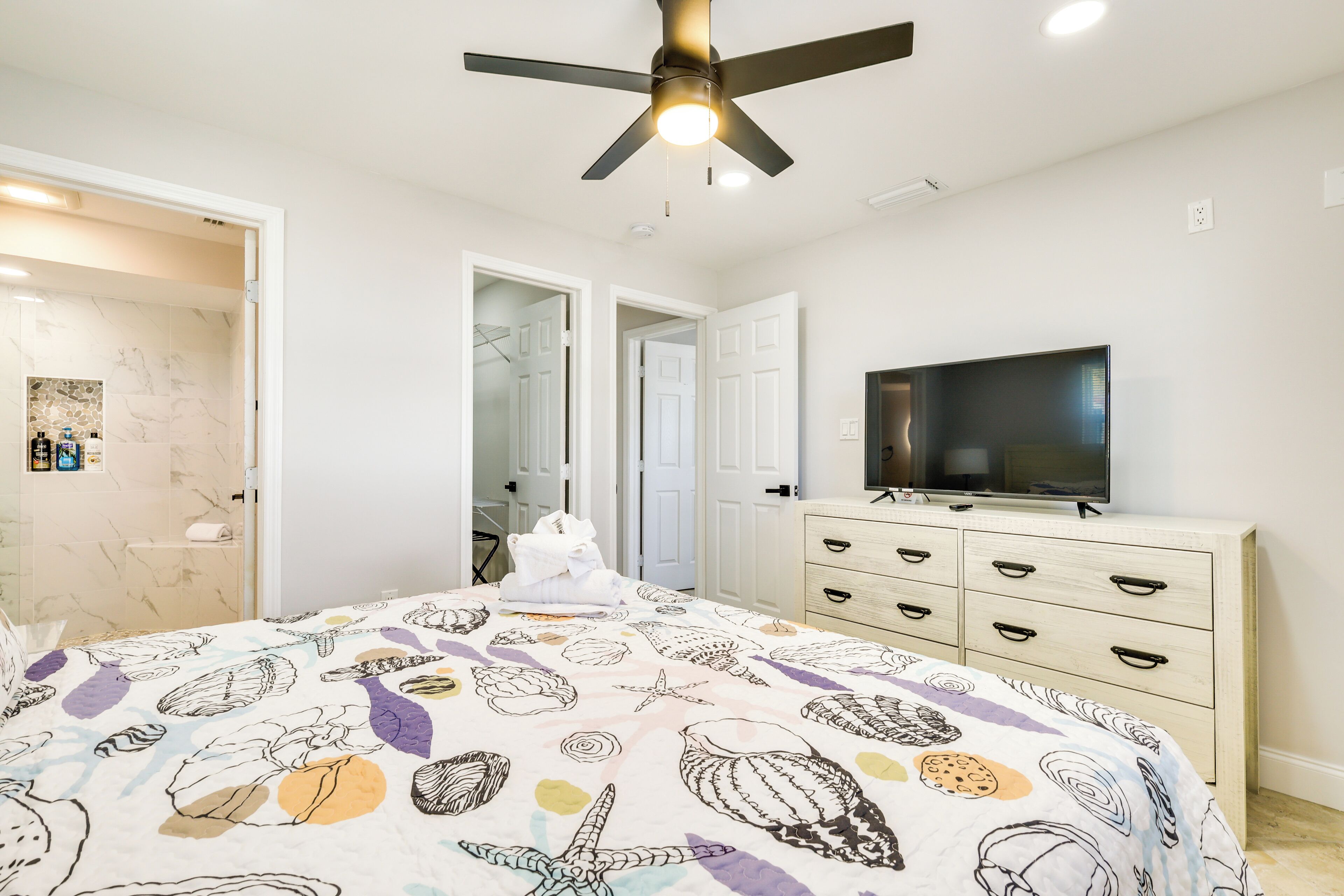 Un dormitorio con cama, ventilador de techo, televisor y cómoda.