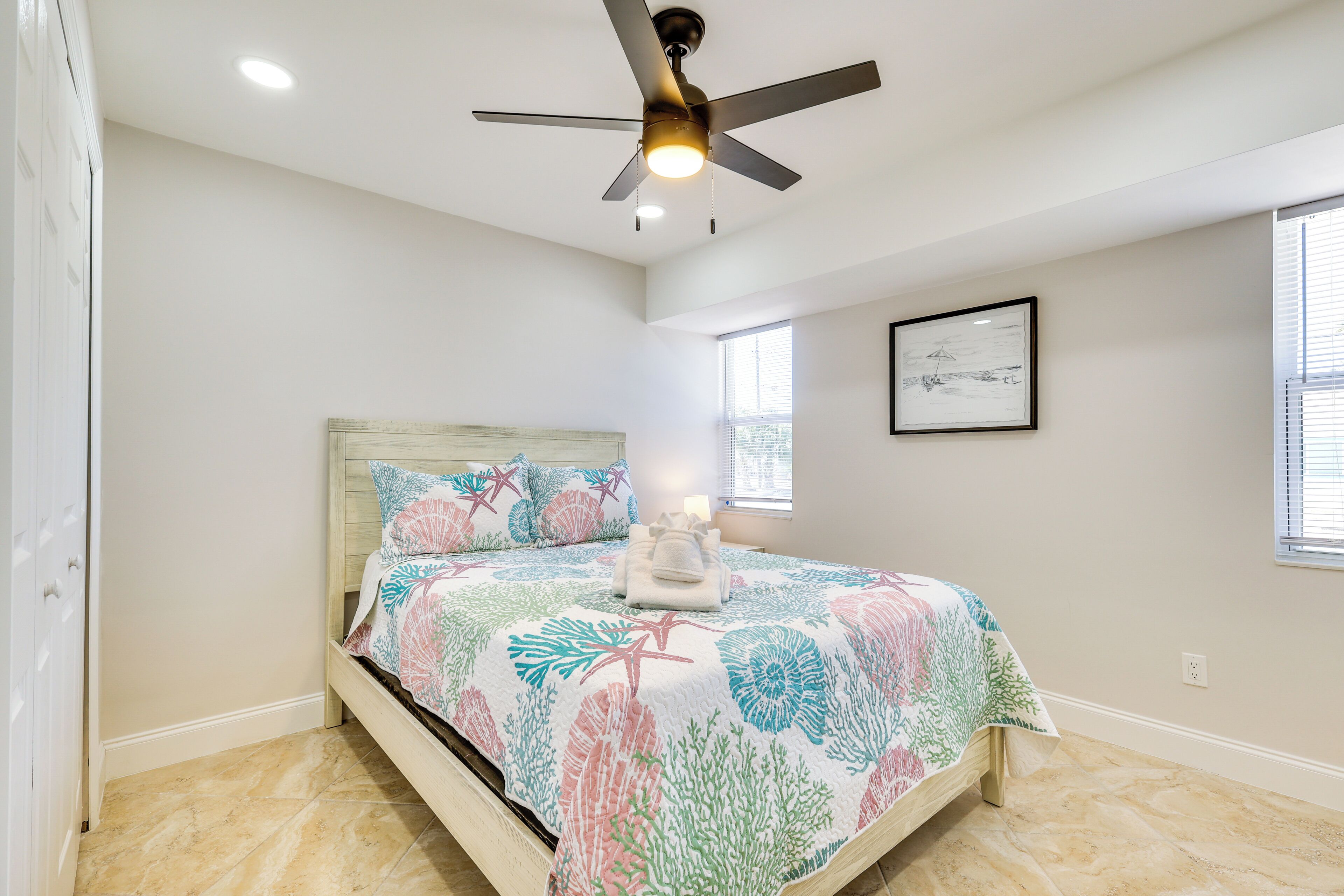 Quarto com cama, ventilador de teto, janela e quadro na parede.