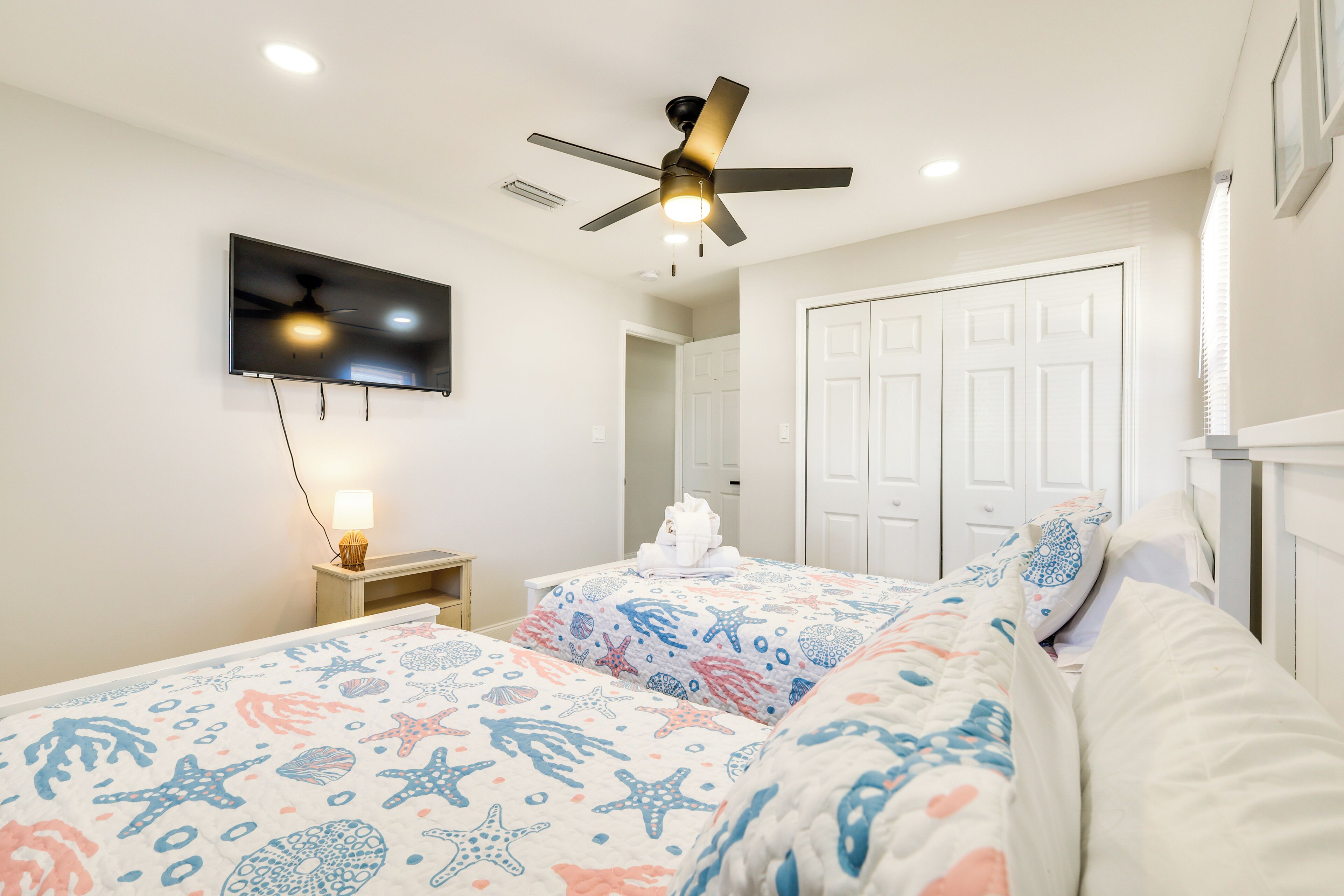 Une chambre avec deux lits, un ventilateur de plafond, une télévision et une porte.