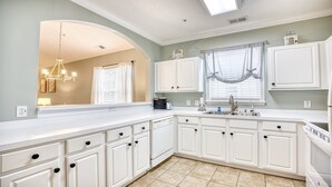 A modern kitchen with white cabinetry, a built-in oven, and a large window with sheer curtains. - 535 Arbor Trace - Barefoot Resort Rentals (North Myrtle Beach)
