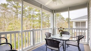 A covered patio with a table and chairs, a ceiling fan, and a view of trees and a house. - 535 Arbor Trace - Barefoot Resort Rentals (North Myrtle Beach)