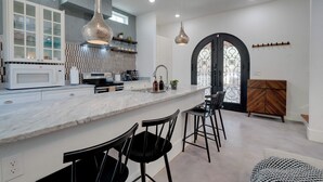 A modern kitchen with a marble countertop, black bar stools, and pendant lighting.