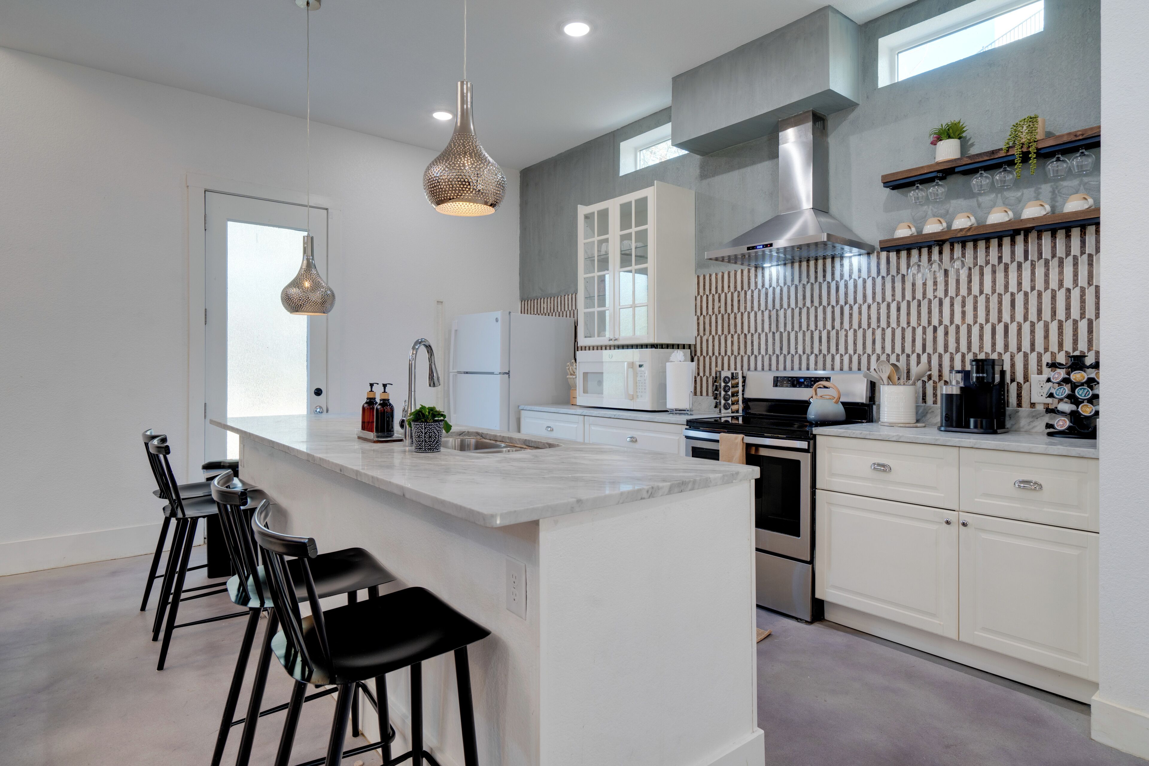 A modern kitchen with white cabinetry, a large island with bar stools, stainless steel appliances, and a hanging light fixture.