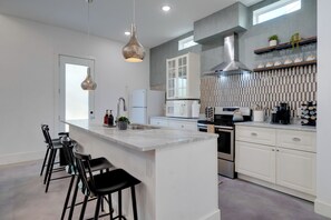 A modern kitchen with white cabinetry, a large island with bar stools, stainless steel appliances, and a hanging light fixture. - Near Lake Travis & Marina: Modern Austin Getaway! (Austin)